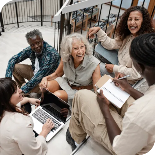 A team gathered around a laptop and a notebook, laughing while they work